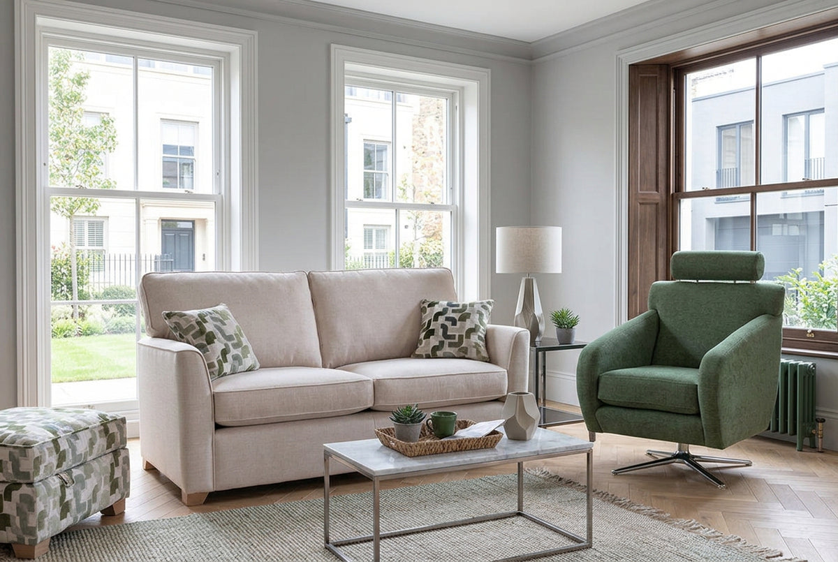 A cream-colored two-seater sofa with two patterned throw pillows, set in a rustic room with stone and wood walls next to a green armchair.