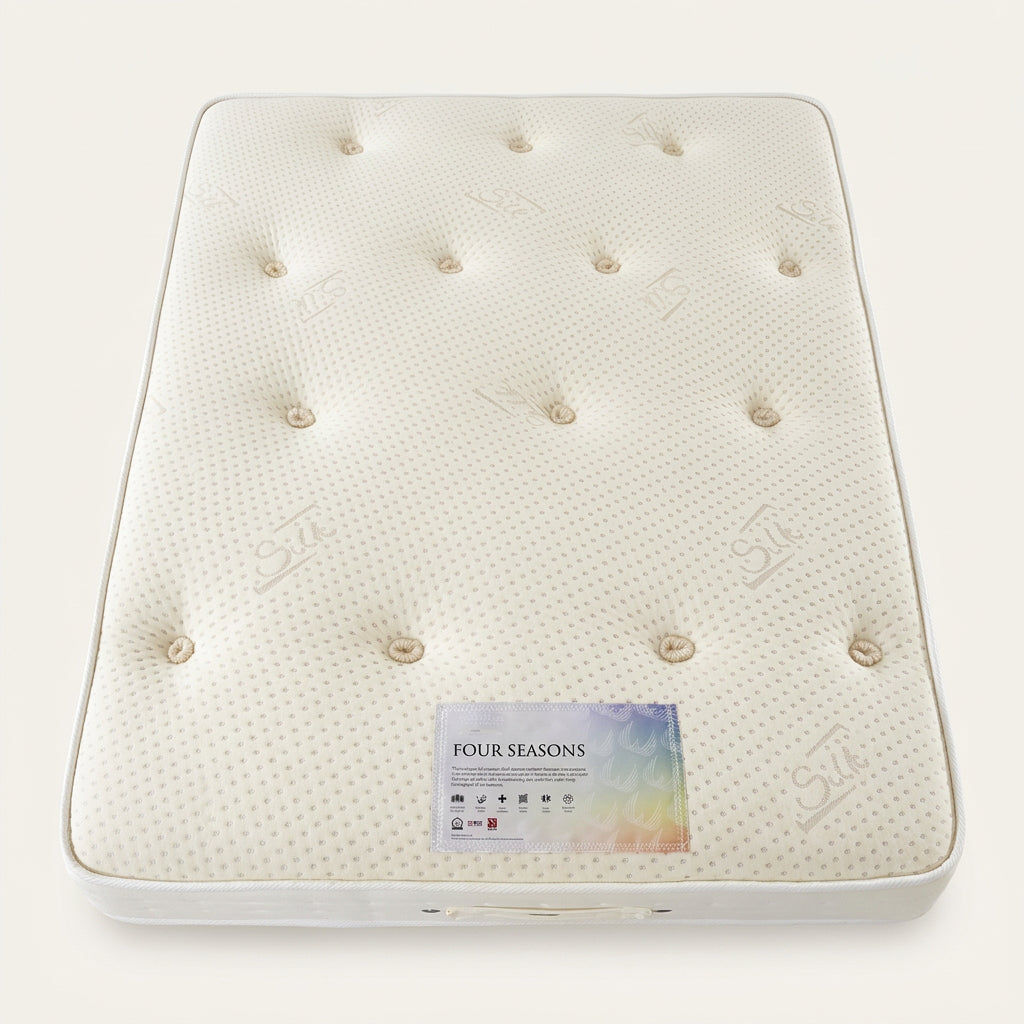A close-up of a white tufted mattress surface with a visible 'FOUR SEASONS' label near the bottom center. The mattress has a dotted texture and button tufting.