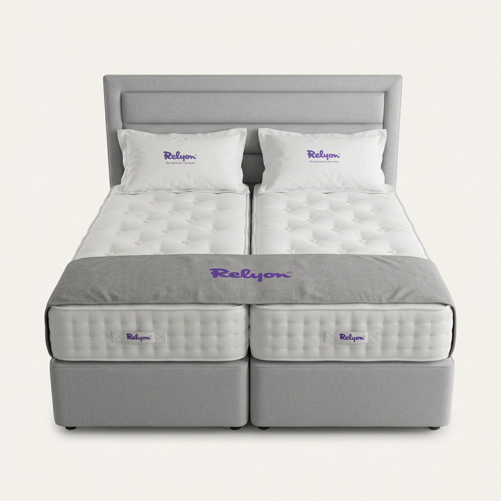 Two side-by-side mattress beds with white tufted mattress toppers, branded pillows, and a grey headboard, displayed in a showroom setting with visible Relyon branding and price tags.