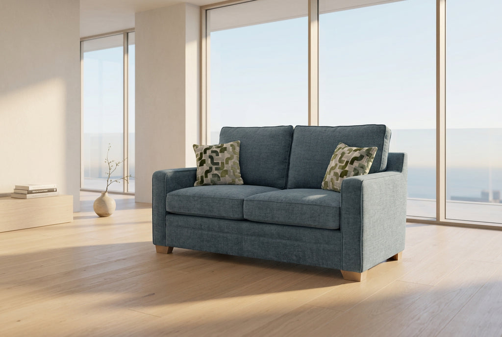 A two-seater upholstered loveseat in textured blue-gray fabric, shown in a furniture store. The sofa has two patterned accent pillows and a small white price tag attached to the backrest.